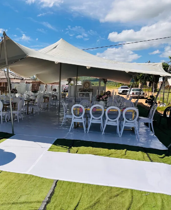 An outdoor wedding marquee with white tables, blush and white centrepieces and a white aisle runner laid over green grass